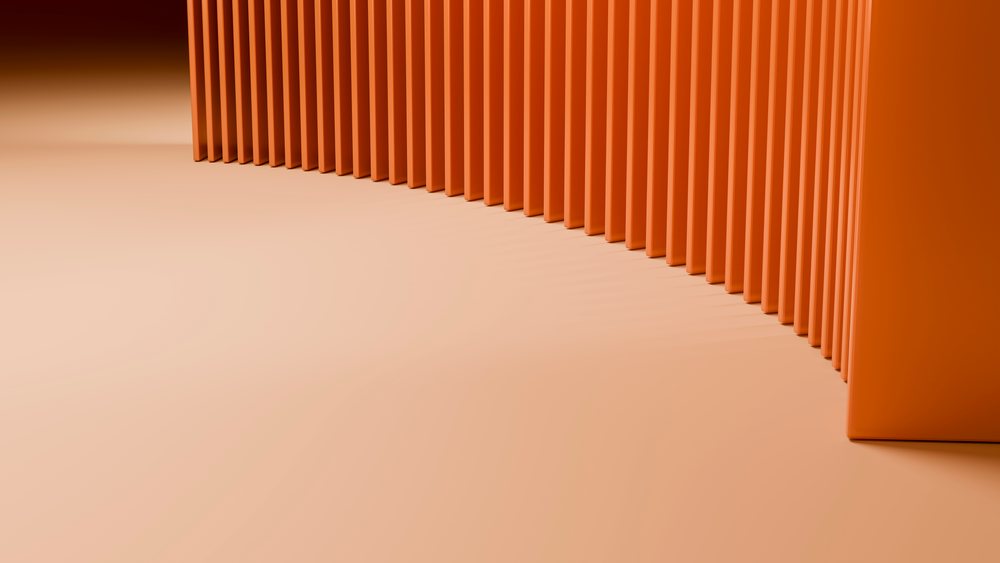Orange vertical panels arranged in a curved formation cast shadows on a flat surface in a minimalist abstract design.