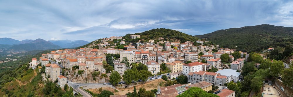 Panoramic view of Evisa village on a hillside with surrounding mountains and a cloudy sky, Travel Photography, Corsica, France.