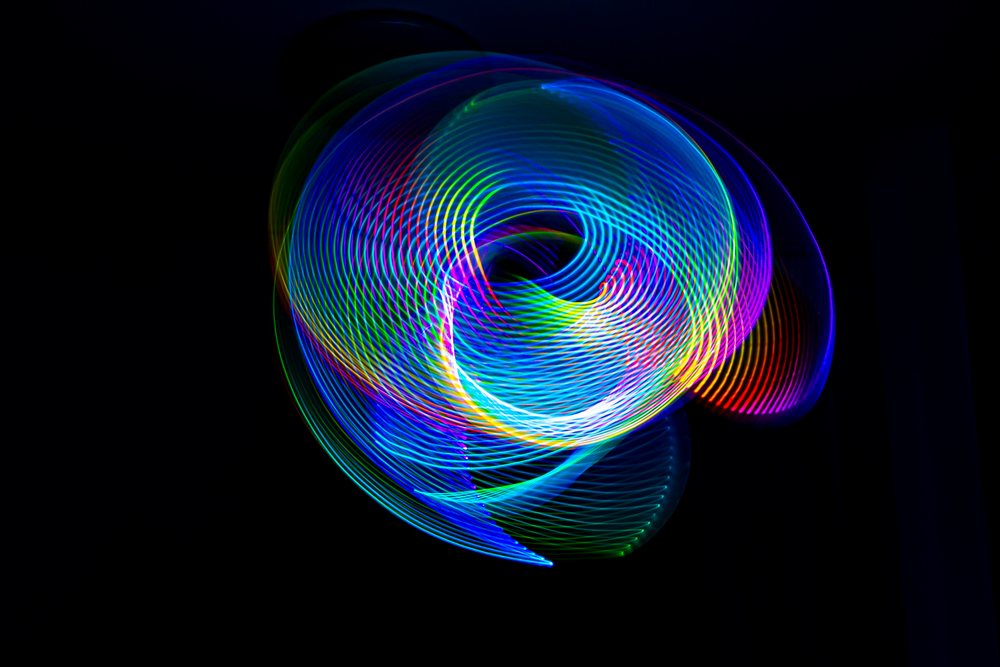 Long exposure photograph of colorful spiral and swirling LED light patterns on a dark background.