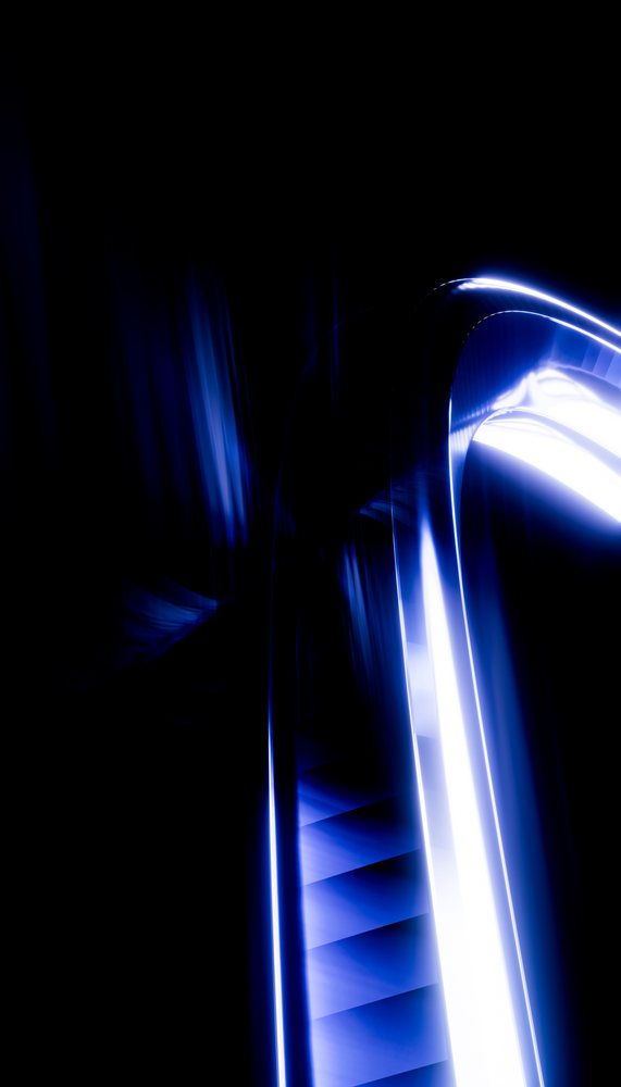 Escalator illuminated with blue light and contrasted against a black background in a modern interior setting.
