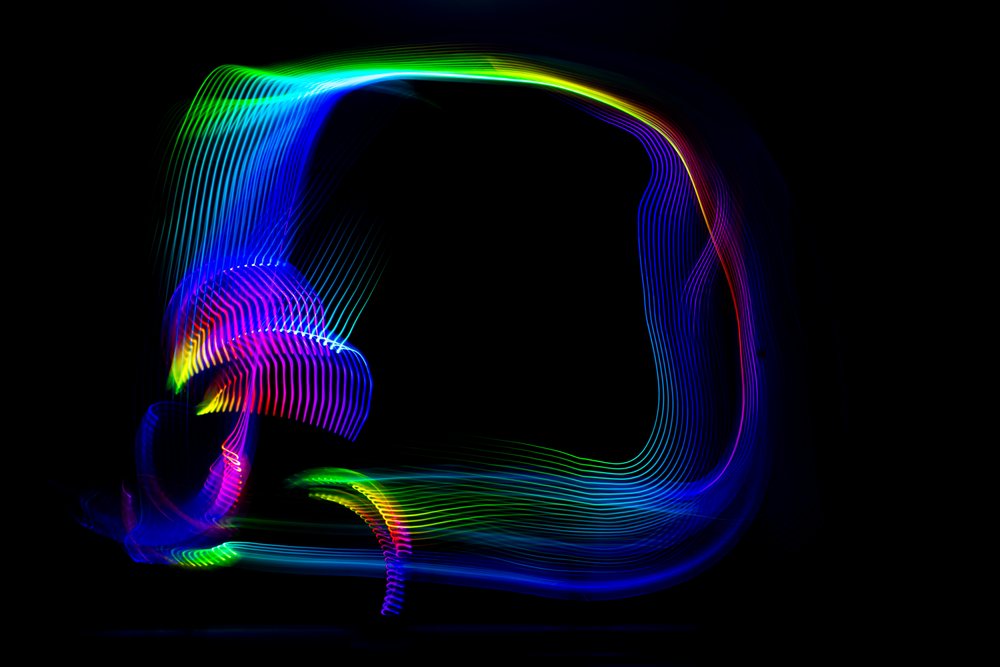 Colorful LED light trails create abstract neon patterns on a dark background in long exposure photography.