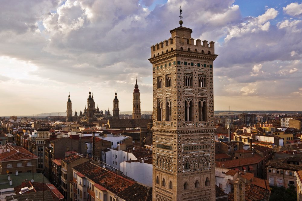 The historic Shrines of the Two Marys tower rises above Zaragoza's urban cityscape under a cloudy sunset sky, Spain.