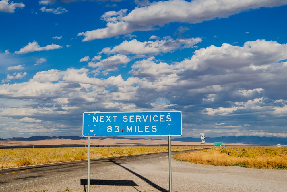 Blue road sign warns of no services for 83 miles on an asphalt highway through a Nevada desert landscape under a partly cloudy sky, USA.