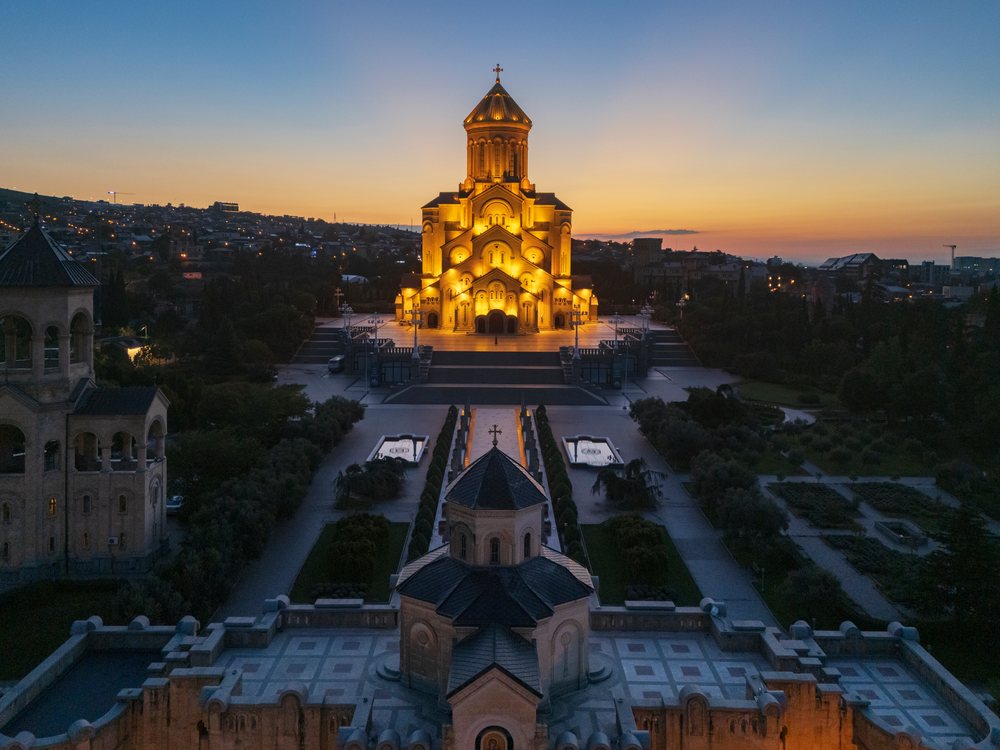 Holy Trinity Cathedral of Tbilisi illuminated at dusk with urban cityscape and skyline, Georgia.