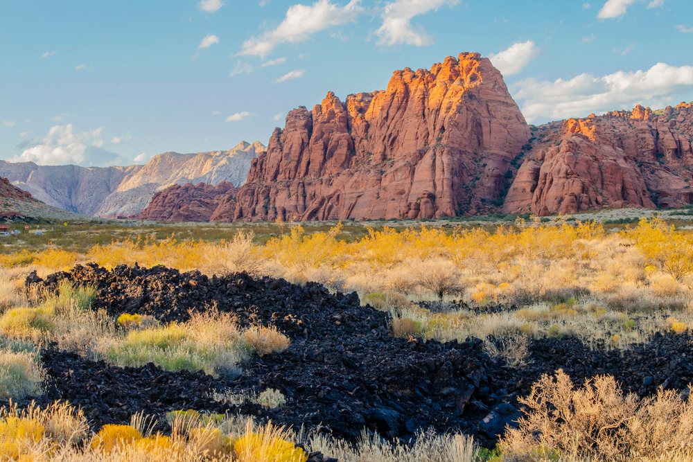 Red rock formations and desert shrubs under a blue sky with clouds at red Cliffs Desert State Park, Snow Canyon, Utah, USA.
