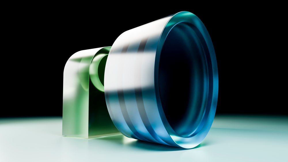 Cylindrical blue-tinted glass lens with green glass block support isolated on dark background under studio lighting.