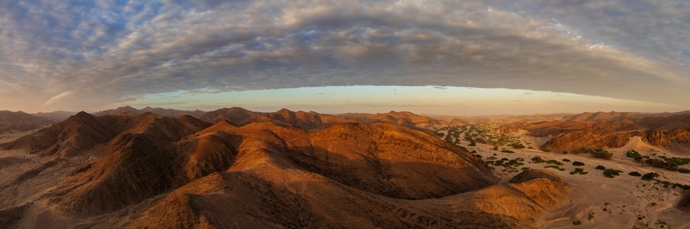 Sunrise over the Hoanib River Valley shows desert mountains, sand dunes, sparse vegetation, and a cloudy sky, landscape, wildlife, Kunene Region, Namibia.