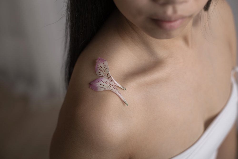 Close-up portrait of a woman's shoulder with two delicate pink flower petals resting on her skin, Art, emotional.