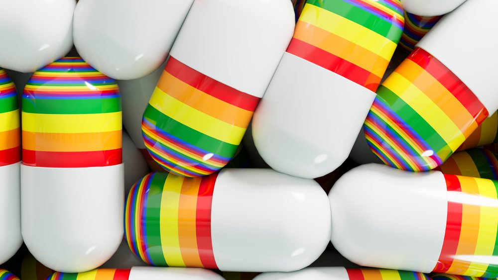 Close-up of shiny, rounded capsules with white and rainbow striped halves packed closely in a pile.
