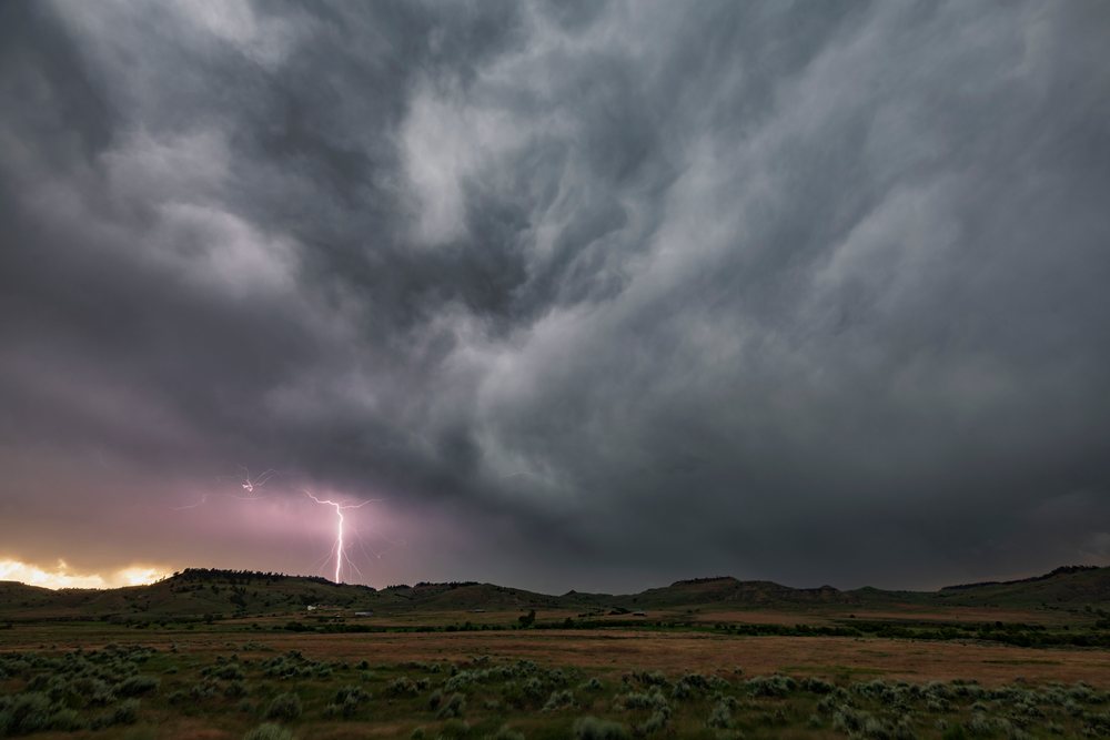 Lightning bolt strikes from dark storm clouds over hills and flat land, Gillette, Wyoming, USA.