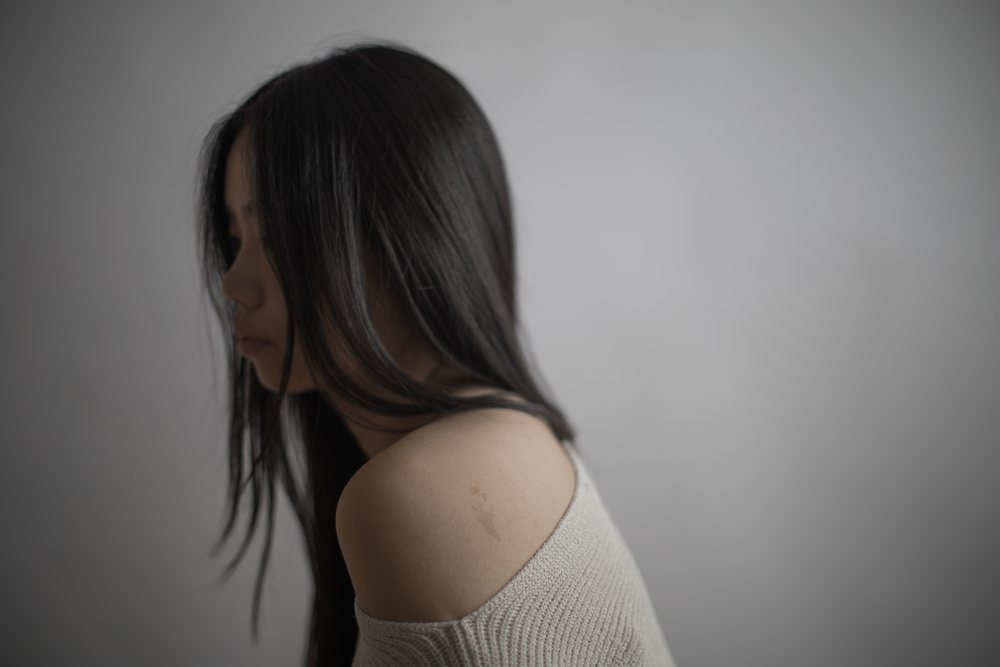 Thoughtful woman with long black hair in an off-shoulder sweater poses emotionally in side profile against a neutral background with soft lighting, Art, portrait, emotional.
