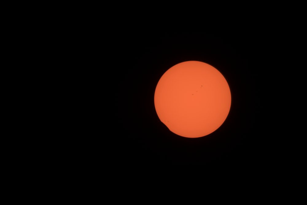 Partial solar eclipse with visible sunspots and orange sun photographed above Los Angeles in the daytime sky, USA.
