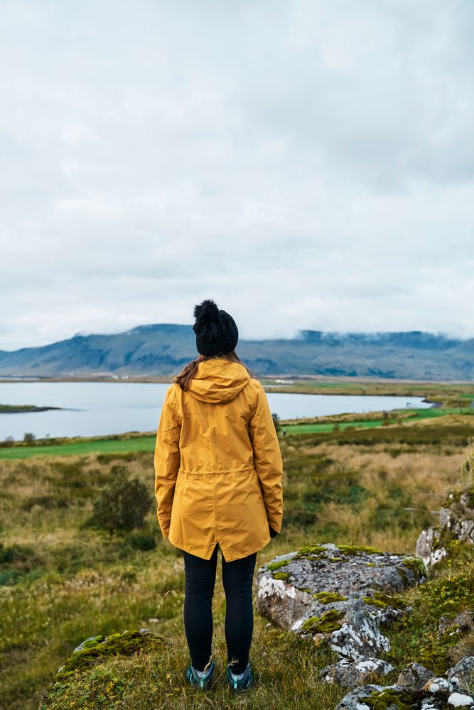 A white woman stands overlooking a scenic lake and mountain landscape