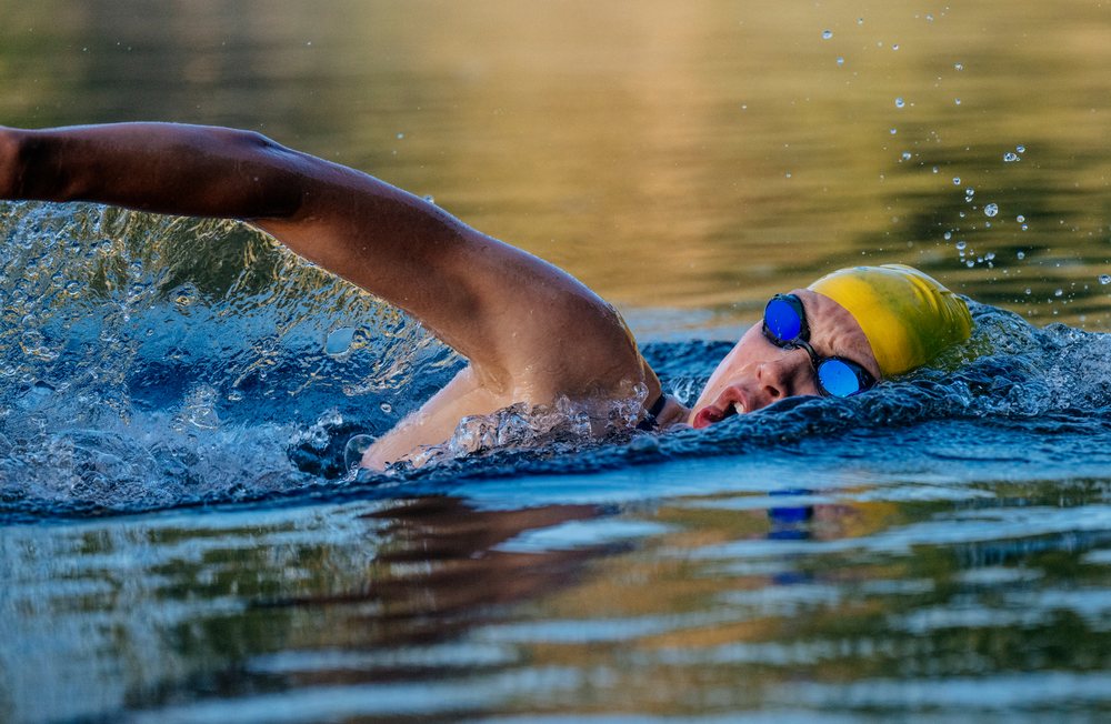 Swimmer wearing a yellow cap and blue goggles performing freestyle stroke in open water, USA.