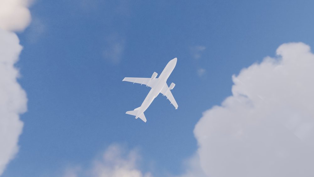 White airplane flying high in a clear blue sky framed by clouds.