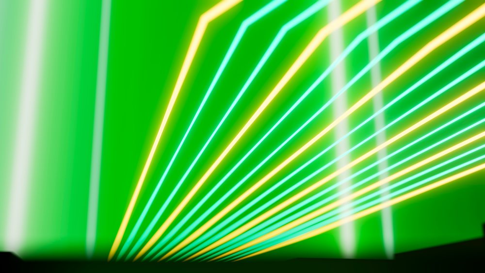 Abstract digital illustration showing green background with neon yellow and blue light beams and rays.