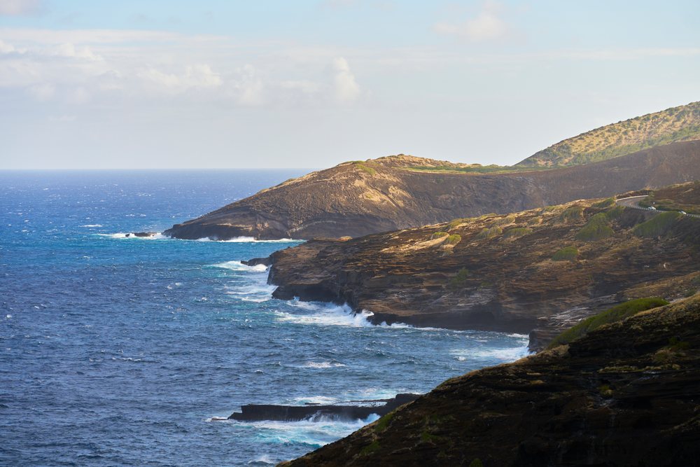 Rocky coastline with ocean waves and a winding road on the hills, Oahu, Hawaii, USA.