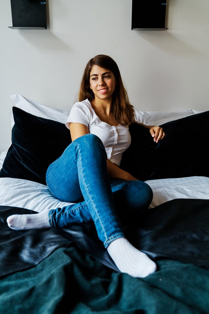 A young woman sitting comfortably on a bed in a modern indoor setting