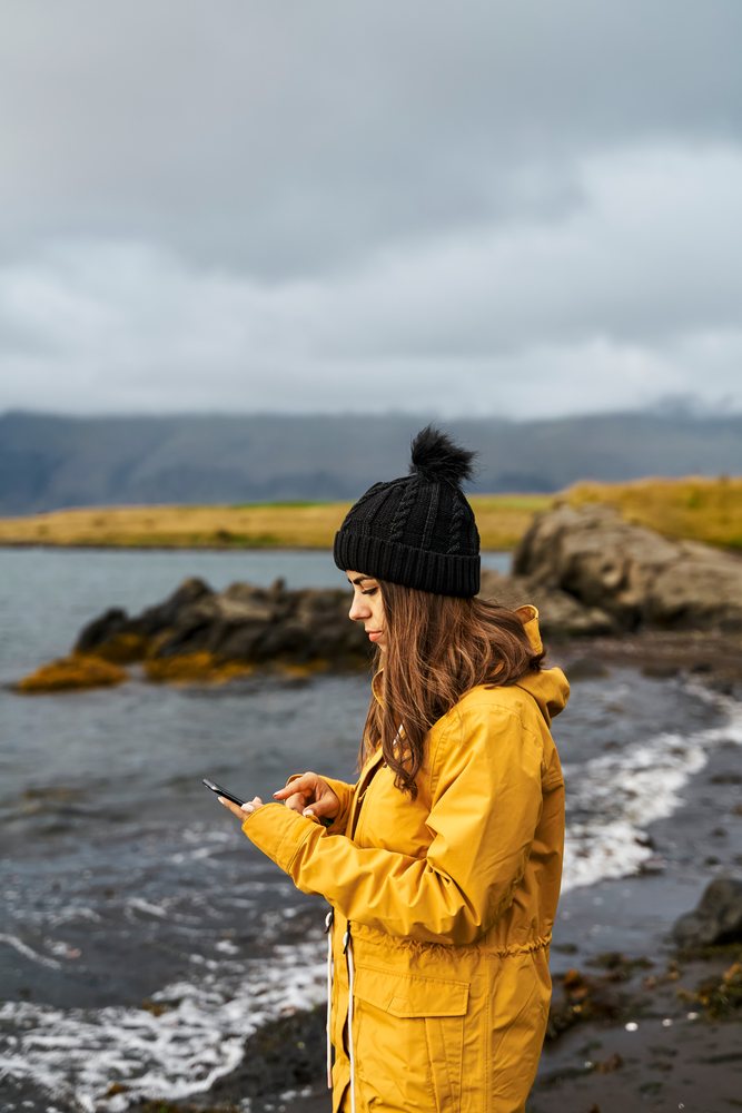 A white woman uses her smartphone by the rocky shoreline