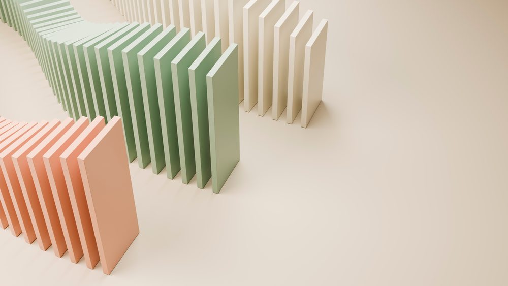 Rows of peach, green, and beige dominoes arranged on a smooth surface for a falling domino effect.