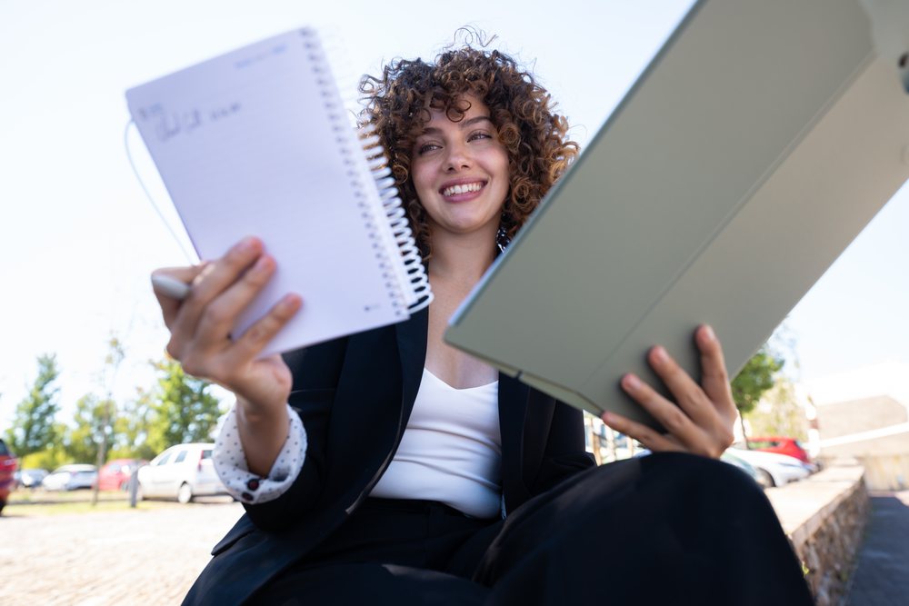 Businesswoman outdoors in Spain holding a notebook and a tablet device while smiling, businesswoman, traveling executive.
