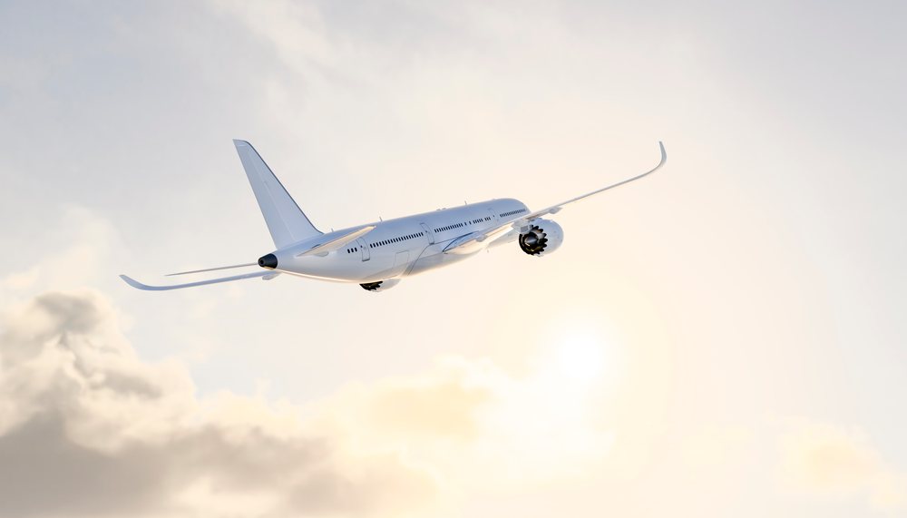 A modern commercial airplane flies in the sky with the sun shining through light clouds, travel, fly, vacation.