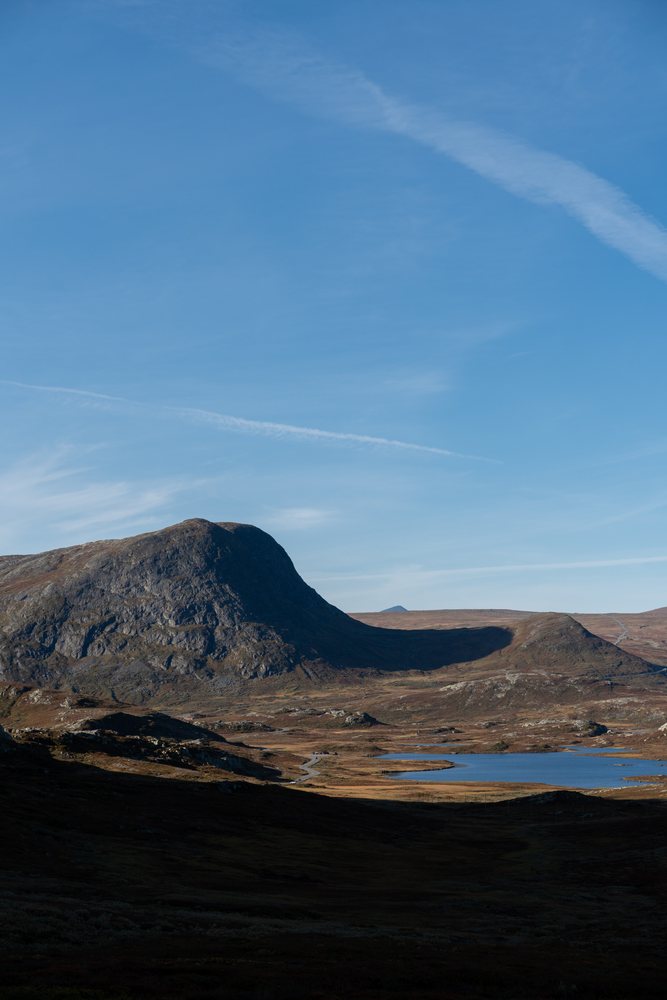 Mountain landscape with lake and winding road under clear blue sky, Norway.