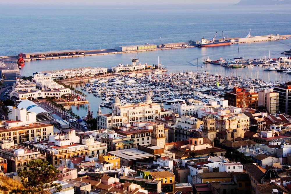 Marina harbor with many boats and yachts moored alongside urban buildings on the coastline at sunset, Costa Blanca, Spain.