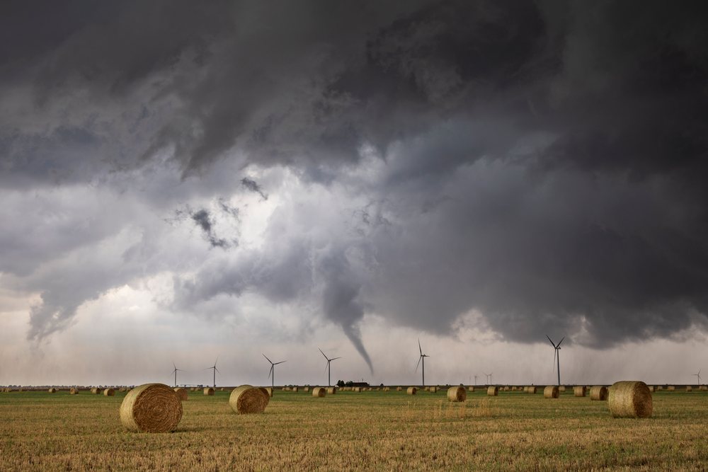 Tornado funnel cloud forms over a rural agricultural field with hay bales and wind turbines, Storm Chasing, Lingo, New Mexico, USA.