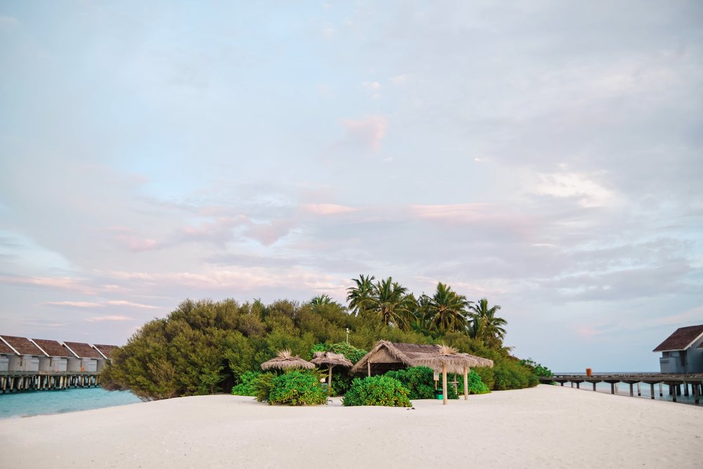 A tranquil tropical island beach with thatched huts and palm trees