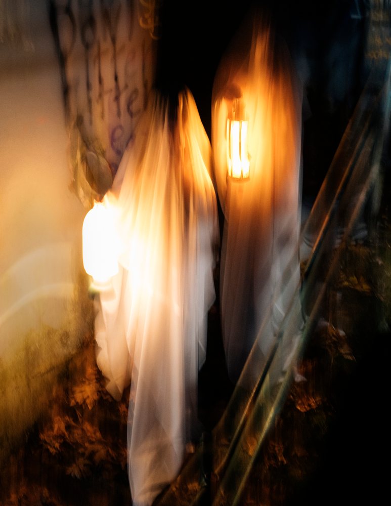 Ghost figures wearing white sheet costumes carry lanterns at night in the USA during a Halloween celebration, ghosts.