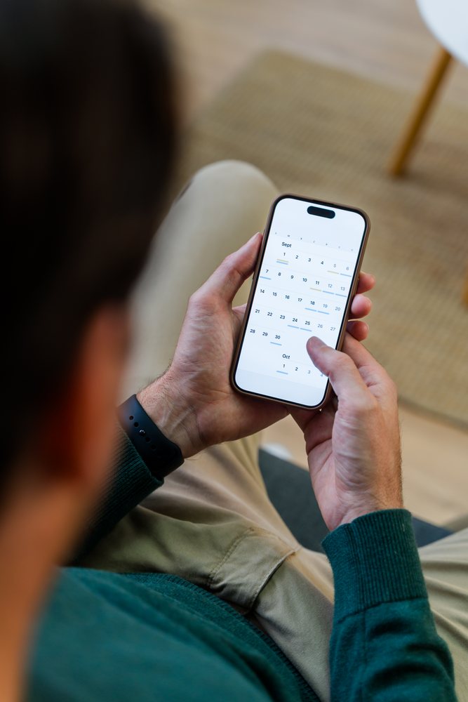 Man seated indoors holding smartphone displaying calendar app while managing his schedule, Spain.