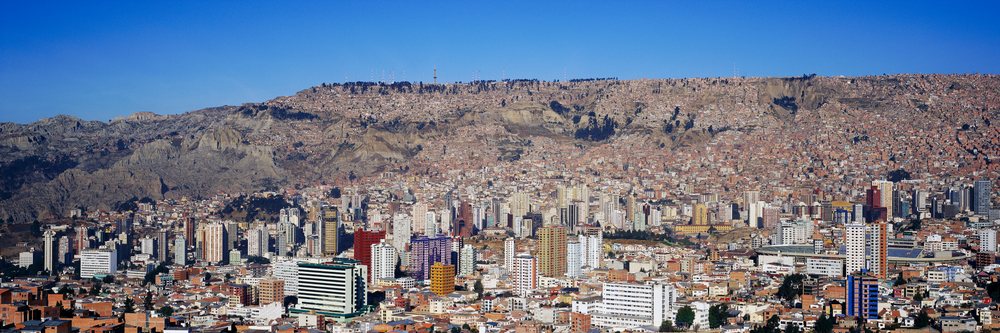 La Paz cityscape showing dense residential and commercial buildings on mountainous terrain under a clear blue sky.