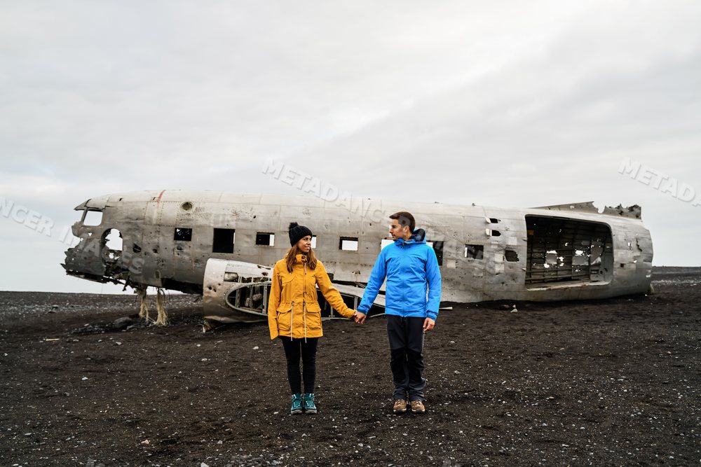 Couple holding hands near a crashed airplane wreck on Iceland's black