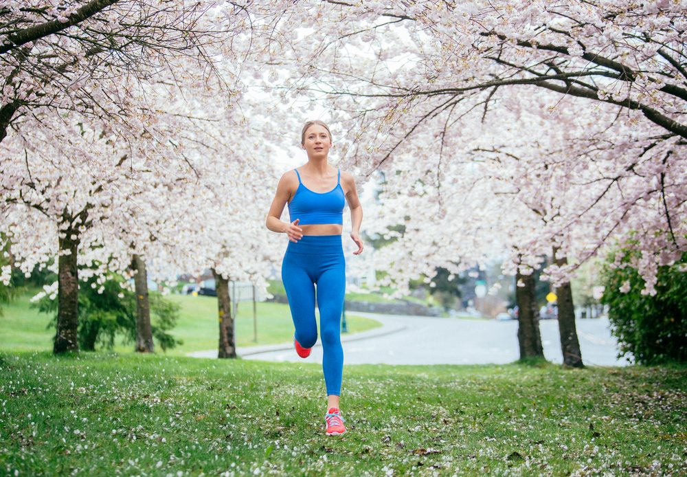Woman running outdoors in a grassy park with blooming cherry blossom trees during spring, USA.