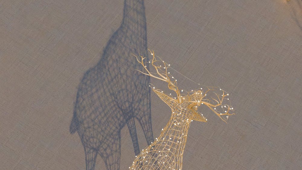 Wireframe deer sculpture with illuminated decorative branches casting a shadow on a textured wall indoors.