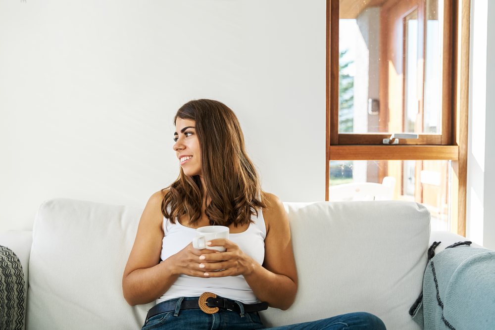 A woman relaxes on a white couch drinking from a mug