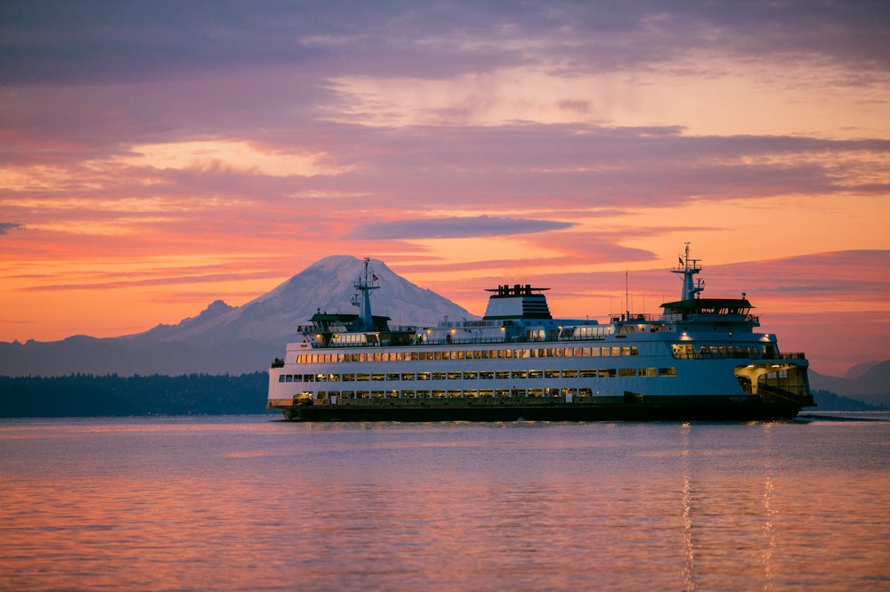 Seattle ferry crosses calm waters near Bainbridge Island at sunset with Mount Rainier in the background, WA, USA.