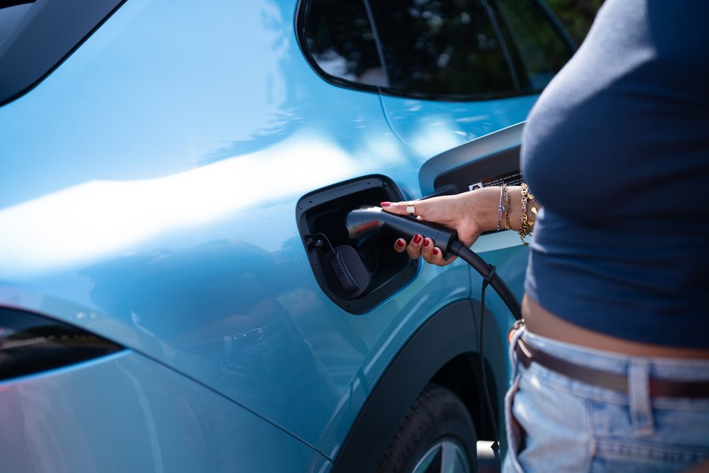 A woman plugs in an electric vehicle to recharge outdoors, green energy, sustainability, mobility, Spain, Europe.
