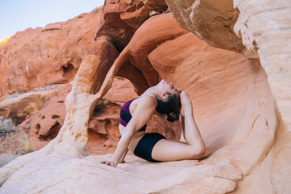 Woman performing a yoga acrobatic pose on a rock formation in a USA desert landscape during summer.