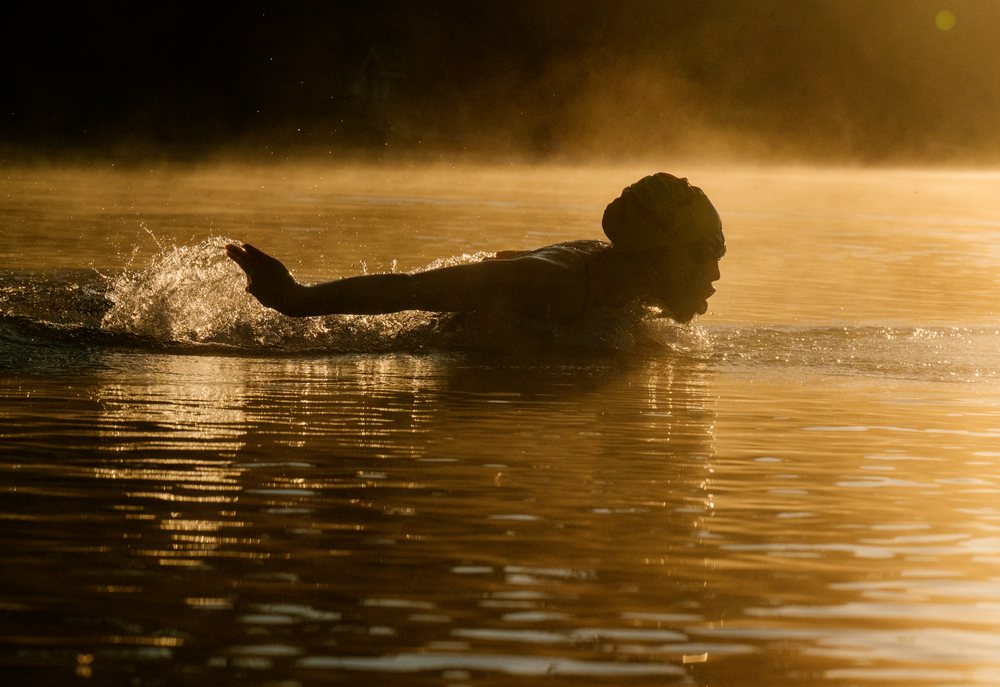 Swimmer executing a stroke in open water during an early morning with the sun casting golden light over the lake, USA.