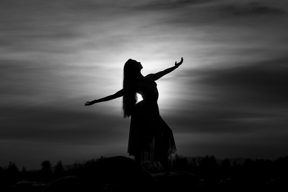 Silhouette of a woman dancer standing outdoors at sunset against a cloudy sky, USA.