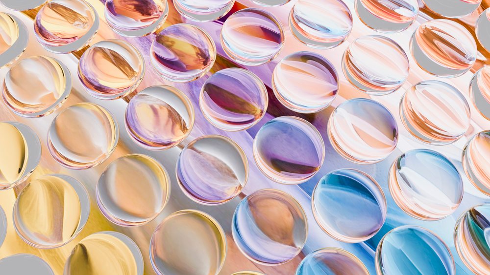 Colorful transparent glass spheres with reflective surfaces arranged in a pattern on a pastel background.