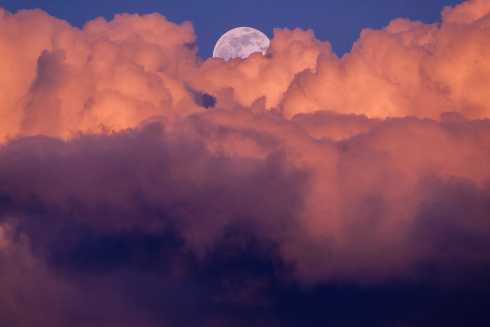 Serene full moon rises behind dramatic orange clouds in a twilight sky over, Seattle, USA.