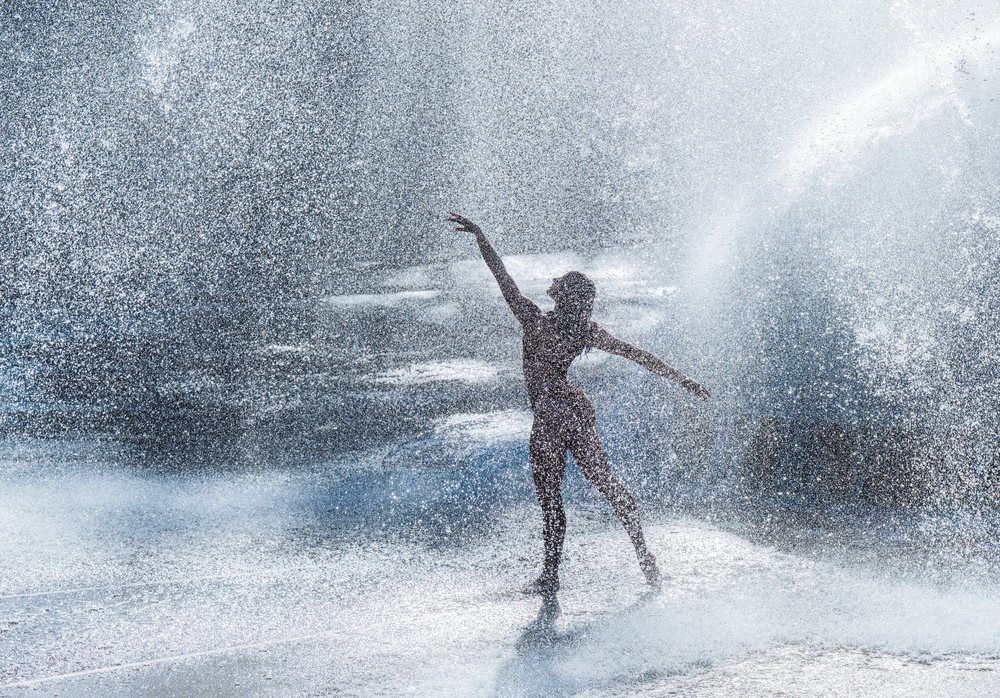 Woman dancing gracefully through splashing water outdoors, partner, acrobatics, yoga, USA.