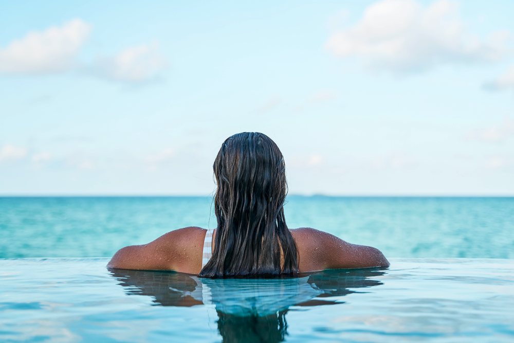 A white woman relaxing in an infinity pool overlooking the ocean