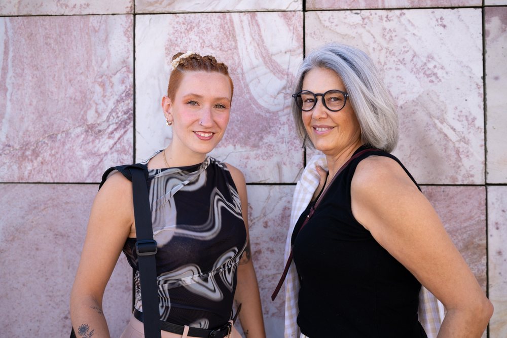 Two women smiling and posing outdoors against a pink marble wall, businesswomen, Spain.