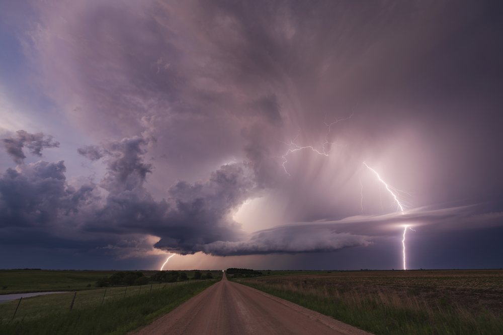 Supercell thunderstorm with multiple Lightning bolts over a rural dirt road and open field at Dusk, Storm Chasing, Weather, Environmental, Jansen, Nebraska, USA.