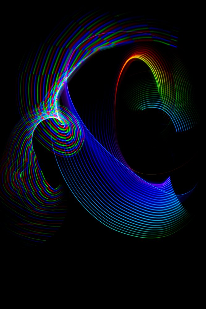Colorful LED light painting with vibrant flowing trails and abstract circular patterns on a black background captured by long exposure photography.