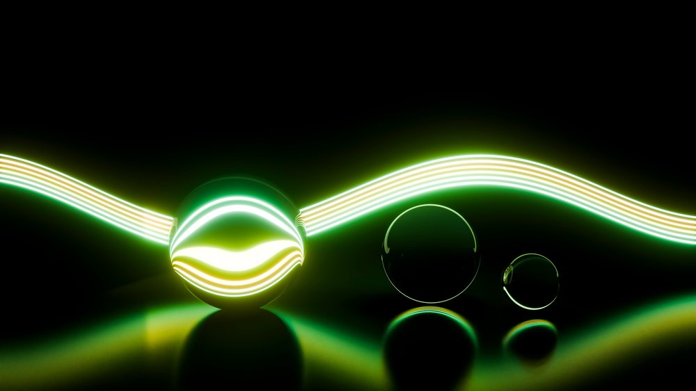 Three glass spheres reflect a glowing neon light wave against a dark background in a studio setting.